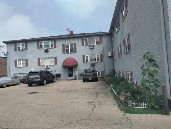 Front view of a three-story apartment building with cars parked in front.