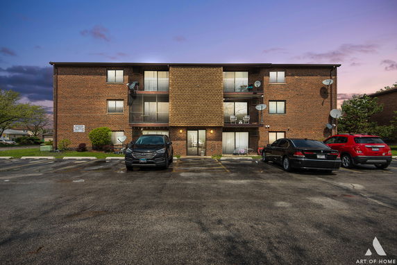 Front view of a three-story brick apartment building with parking area.