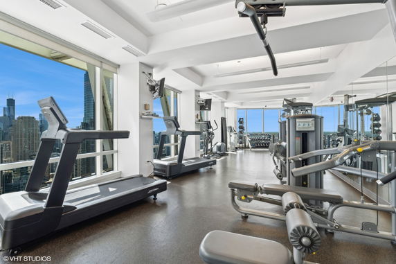 Indoor gym with exercise equipment and large windows displaying a city view.