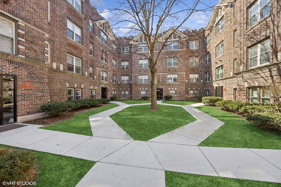 Front view of a multi-story brick residential building surrounding a landscaped courtyard.