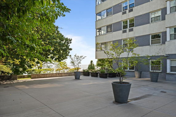 View of the side of a multi-story building with large windows and potted plants on a spacious patio area.