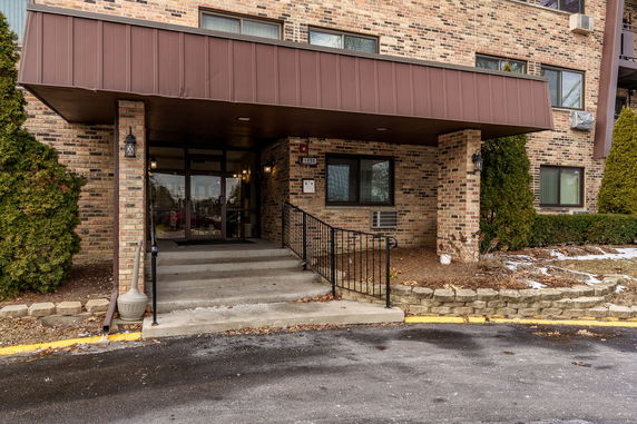Front view of a brick apartment building entrance with steps and railing.