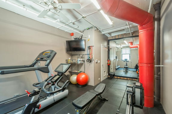 Indoor gym area with fitness equipment and large red ventilation pipes.