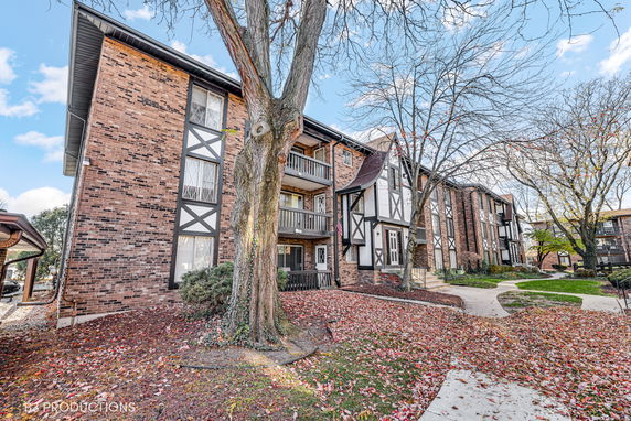 Front view of a multi-story brick apartment building with balconies, featuring a Tudor-style architectural design.