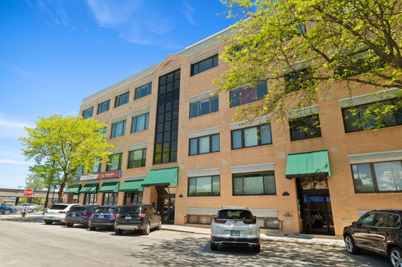 Front view of a four-story brick building with green awnings and large windows.