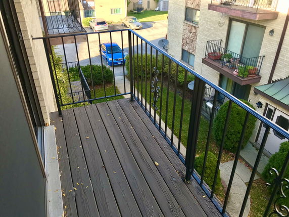 View from a balcony overlooking a small parking area and neighboring buildings.
