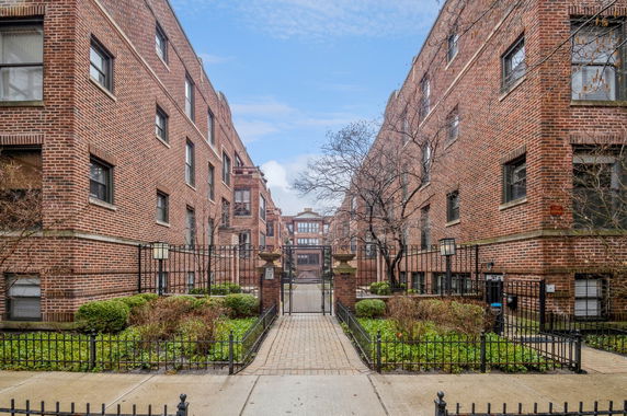 Front view of a multi-story brick apartment building with a gated entrance.