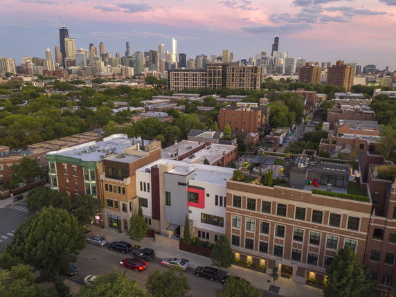Aerial view of city buildings with a skyline in the background under a colorful sky.