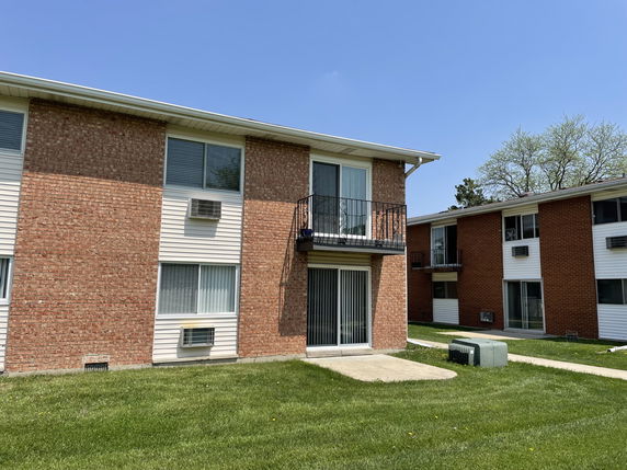 Front view of a two-story apartment building with a balcony and sliding glass doors.