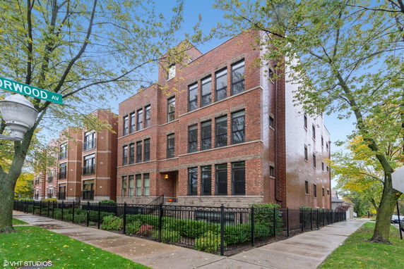 Front view of a multi-story brick building with several windows and a fenced sidewalk.