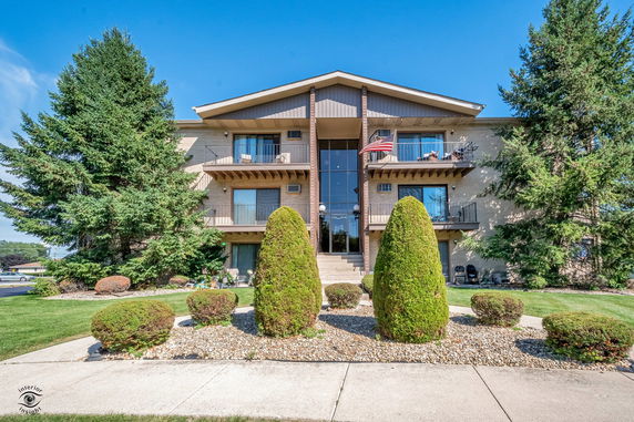 Front view of a multi-story apartment building with balconies and a landscaped entrance.