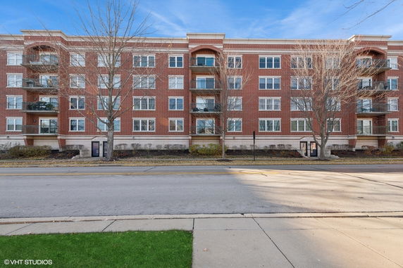 Front view of a four-story brick apartment building with balconies and numerous windows.