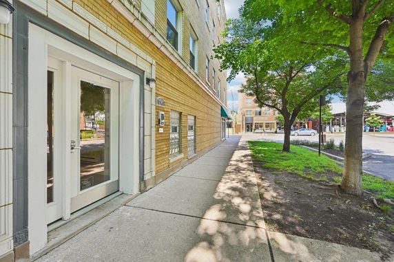 Front view of a multi-story brick building with glass entrance doors and sidewalk.