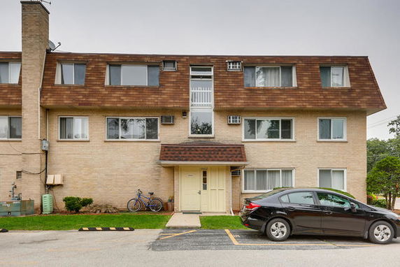 Front view of a three-story apartment building with a brown roof and light brick exterior.