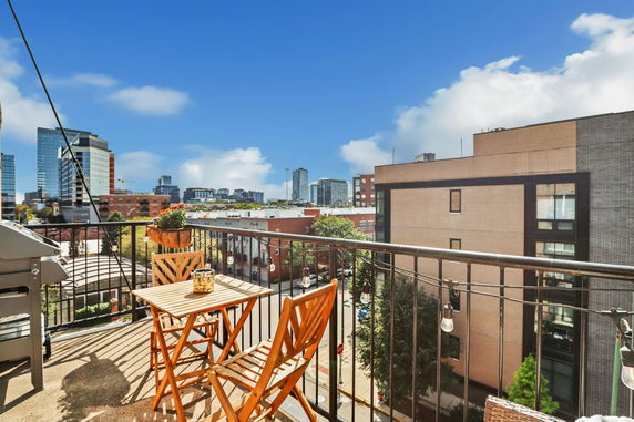 Panoramic view of a cityscape from a rooftop balcony with seating and a grill.