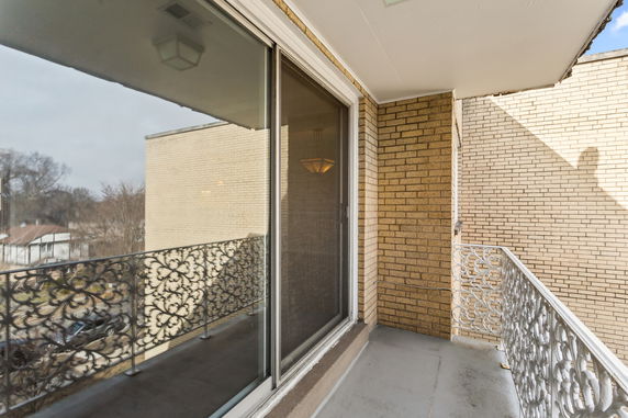 Balcony with decorative railing overlooking a brick building and trees.