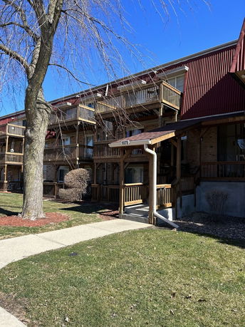 Front view of a multi-story residential building with wooden balconies and a metal roof.