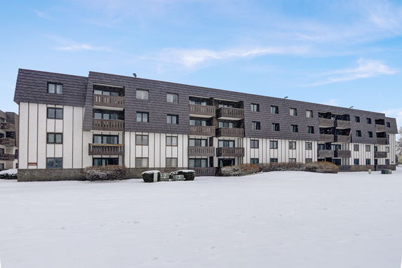 Front view of a multi-story apartment building with balconies and a snowy landscape.