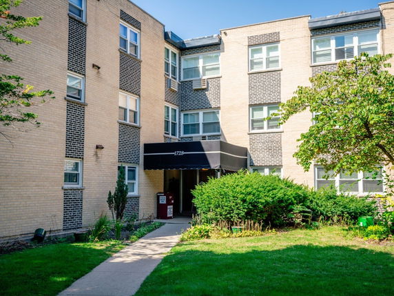 Front view of a three-story apartment building with a brick exterior and a black awning entrance.