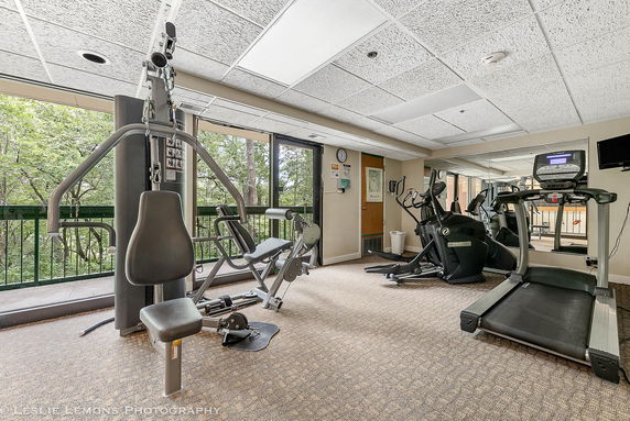 Interior view of a fitness room with gym equipment and large windows.