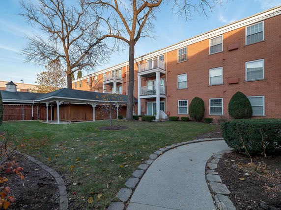 Front view of a multi-story brick apartment building with balconies and a landscaped front area.