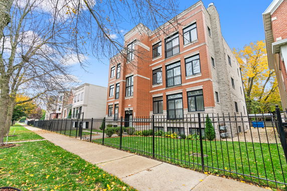 Front view of a multi-story brick building with black framed windows and a fenced yard.