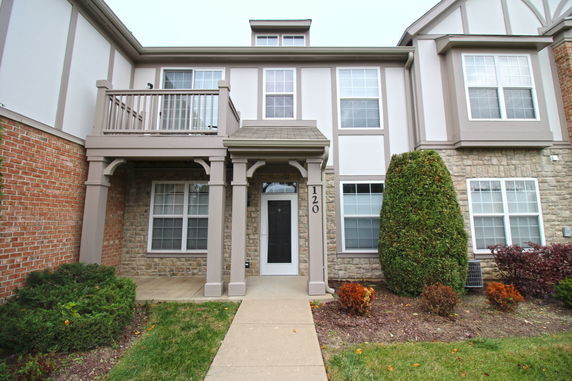 Front view of a two-story house with a balcony and brick facade.
