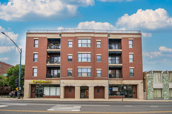 Front view of a multi-story brick building with balconies and a street-level shop.