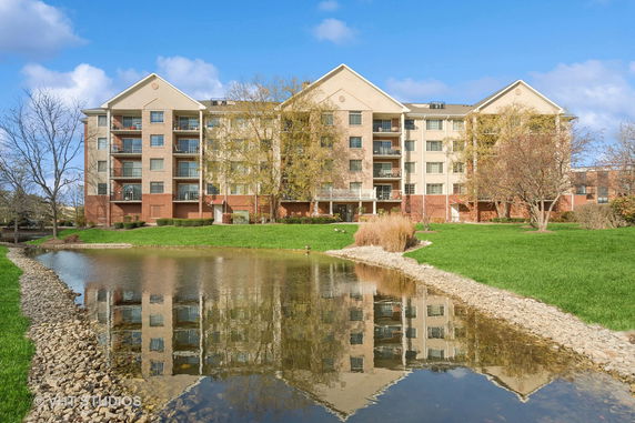 Front view of a multi-story apartment building with balconies and a pond in the foreground.