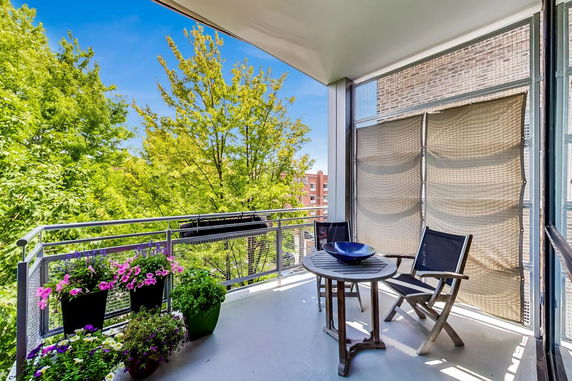 Balcony with chairs and table, overlooking trees and nearby buildings.