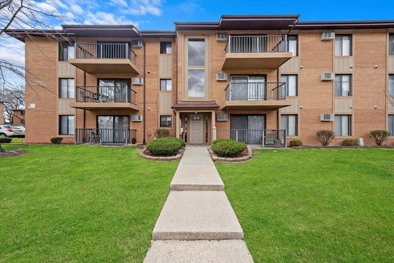 Front view of a multi-story residential building with balconies and a central entrance.
