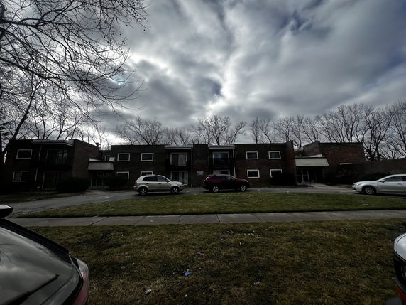 Front view of a two-story apartment building with multiple units and a parking area in front.
