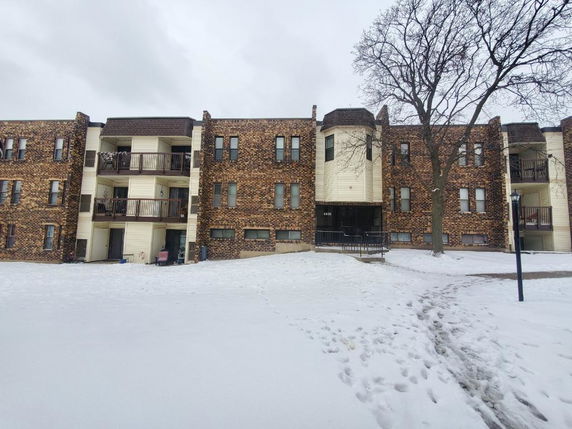 Front view of a multi-story brick apartment building with balconies and snow-covered ground.