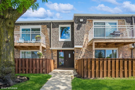 Front view of a two-story apartment building with balconies and a wooden fence.