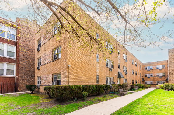 View of a multi-story brick apartment building with multiple windows and air conditioning units.