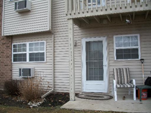 Front view of a building with siding, windows, a door, and a small outdoor seating area.