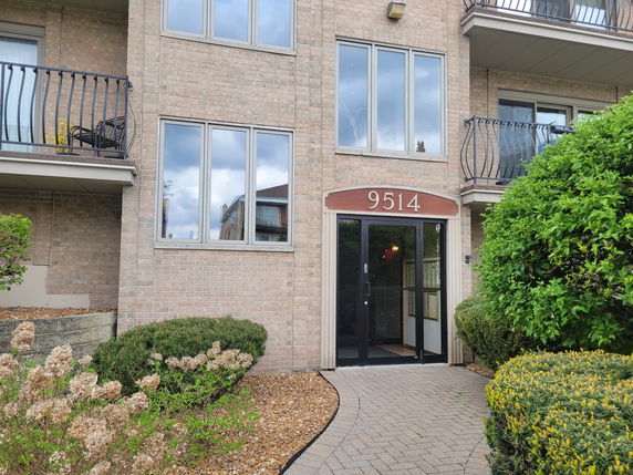 Front view of a multi-story brick building with balconies and entrance.