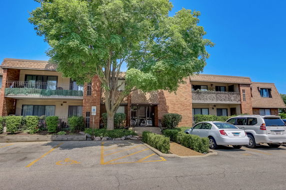 Front view of a two-story brick apartment building with balconies and parking spaces in front.