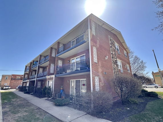 Front view of a three-story brick apartment building with balconies.