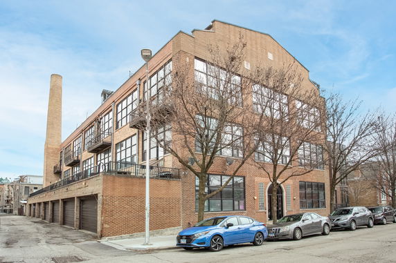 Front view of a multi-story brick building with large windows and a chimney.