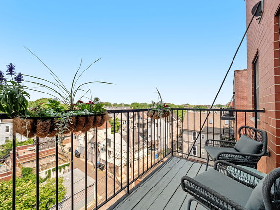 View from a balcony with outdoor furniture and potted plants overlooking residential buildings.