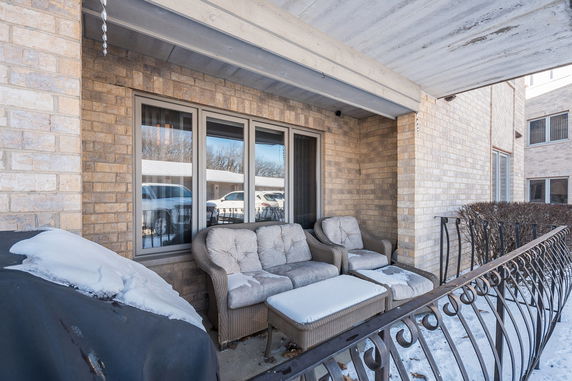 View of a brick building with a balcony featuring outdoor furniture and a snow-covered railing.