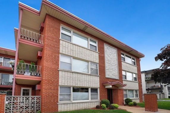 Front view of a three-story brick apartment building with balconies.