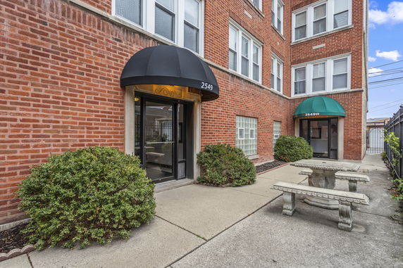 Front view of a brick apartment building with black and green awnings over entrance doors.