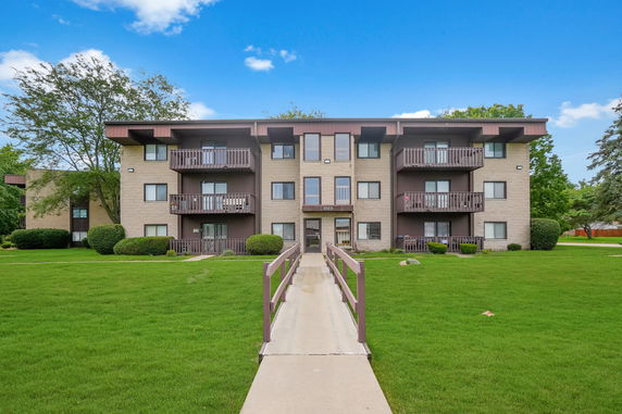 Front view of a three-story apartment building with balconies and a pathway leading to the entrance.