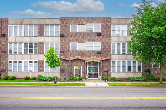 Front view of a three-story brick and concrete apartment building with large windows.