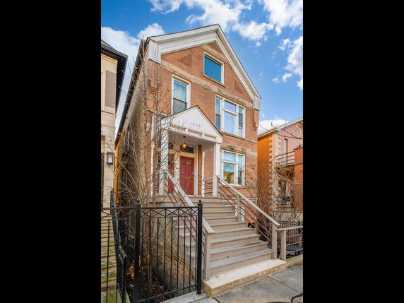 Front view of a two-story house with a red door and steps leading to the entrance.