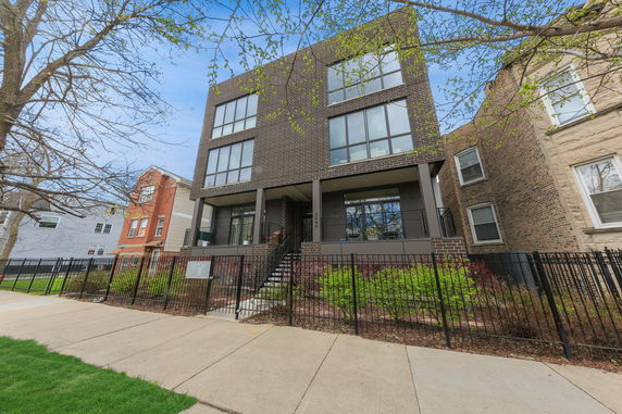 Front view of a modern multi-story building with large windows and a fenced yard.
