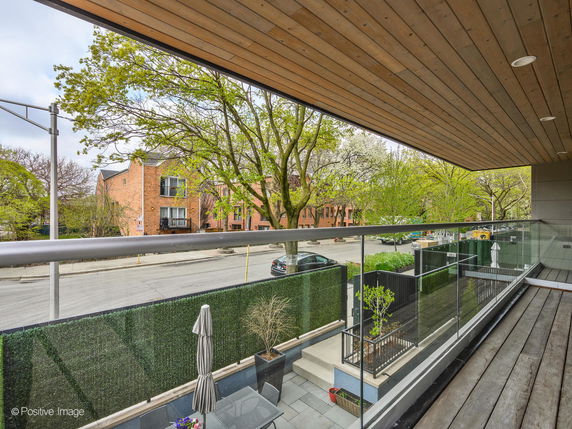 Panoramic view from a building's balcony showing a street and surrounding trees.
