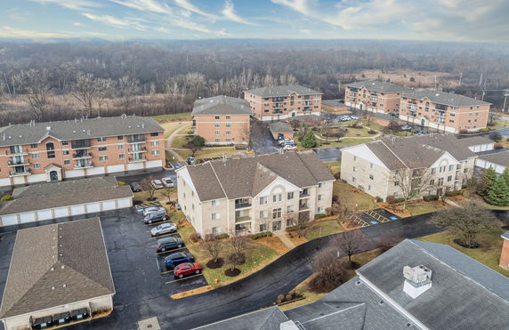 Aerial view of residential apartment buildings with parking lots and surrounding wooded areas.